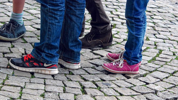 Kinderfüße in bunten Turnschuhen, die auf einem Kopfsteinpflaster stehen.