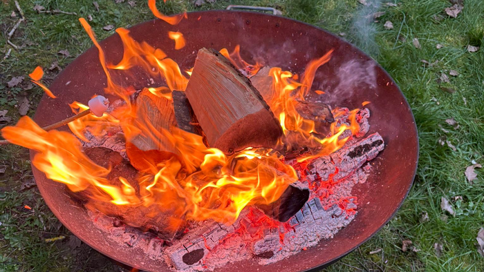 Ein tragbarer Grill mit glühender Kohle und Holzscheiten auf einer grasbewachsenen Fläche im Freien.