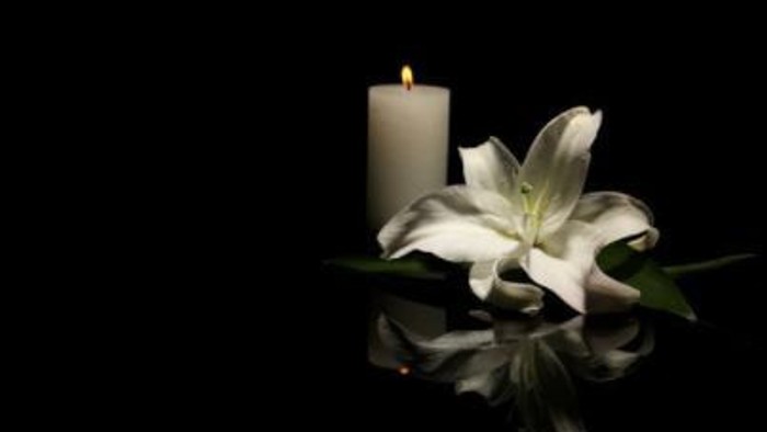 A single lit candle next to a white lily on a dark background