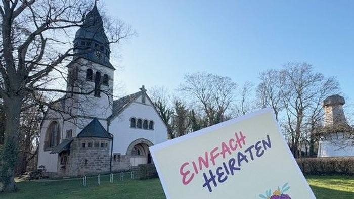 Eine Kirche und im Vordergrund das Plakat der Aktion Einfach heiraten