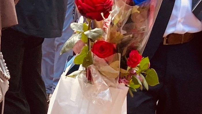 Konfirmand i jakkesæt med pose i hånden fuld af røde og blå roser, mange folk i baggrunden på forpladsen ved Tornbjerg Kirke (ingen ansigter kan ses)