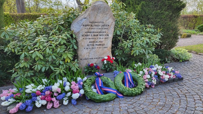 En mindesten med blomsterarrangeringer og bænder på en stenvej.