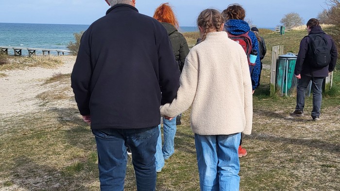 Gruppe af mennesker, der går langs en kyststi nær havet på en klar dag.