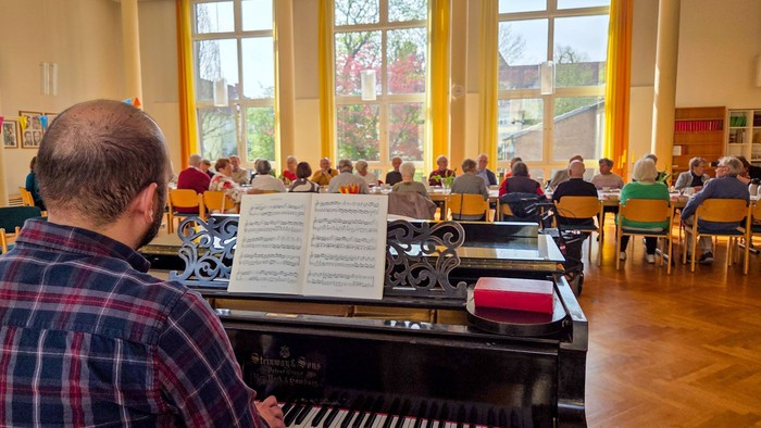 Ein Mann, Kreiskantor Jozsef Opicz, spielt am Klavier vor einer langen Tafel mit älteren Menschen
