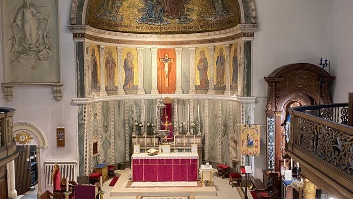 Elegante Kircheninnenausstattung mit prunkvollem Altar, Buntglasfenstern und hölzernen Kirchenbänken mit reichen Verzierungen.
