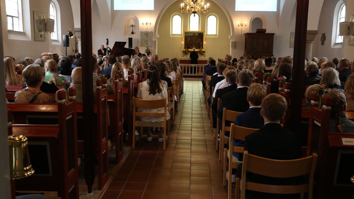 En overfyldt kirkeindretning med deltagere, der sidder og vender mod alteret under en gudstjeneste.