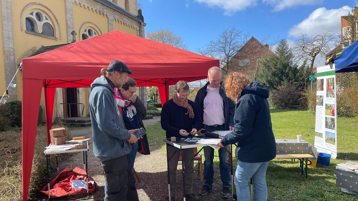 Fünf Leute stehen am Stand mit roten Zelt und Informationen zur Biodiversität. Es findet ein Gespräch statt.