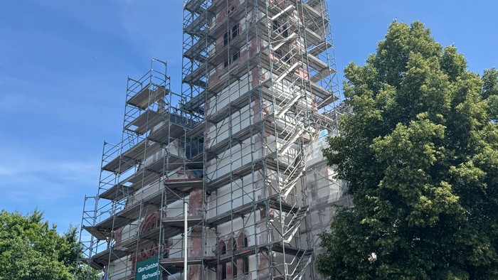 Historische Kirche mit umfangreicher Gerüstkonstruktion für Restaurierungsarbeiten vor klarem blauem Himmel.