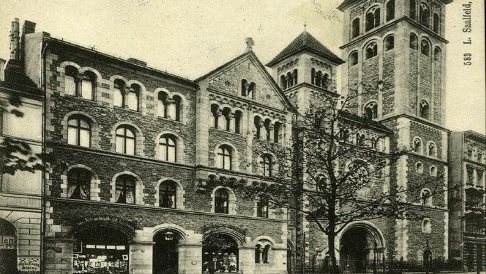 Altes Gebäude mit hohem Turm und vielen Fenstern, Menschen auf Kopfsteinpflasterstraße