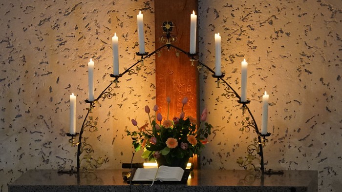 Bild zeigt eine Kirchenbank mit brennenden Kerzen und einem Blumenstrauß