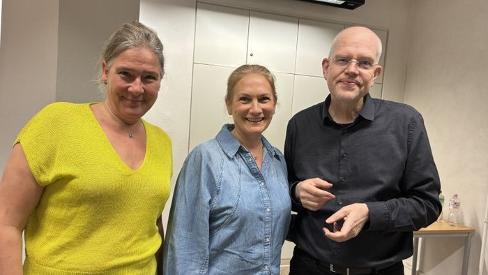 Drei Personen, die gemeinsam in Innenräumen lächeln, während einer scheinbar lockeren oder beruflichen Zusammenkunft.