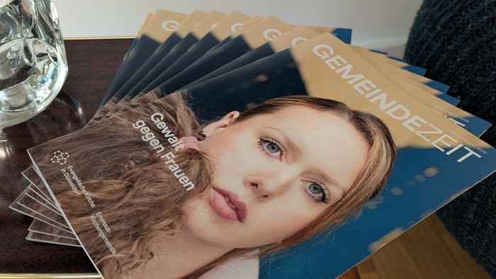 Zeitschriftenstapel mit einem Cover, das eine Frau zeigt und die Aufschrift „Gemeindezeit“ trägt, auf einem Holztisch.