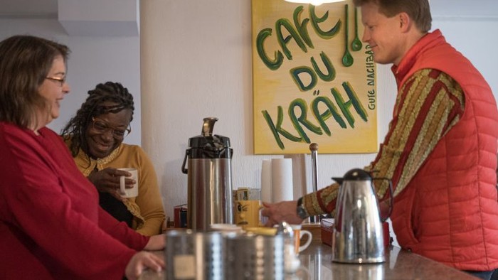 Menschen genießen Kaffee in einem gemütlichen Café namens „Café du Kräh“ mit entspannter, geselliger Atmosphäre.