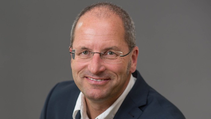 Kopf und Oberköper von Norbert Mecke, der vor einem neutralen Hintergrund sitzt