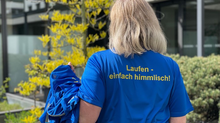Frau mit Laufshirt, Laufen - einfach himmlisch, und weitere Shirts über dem Arm