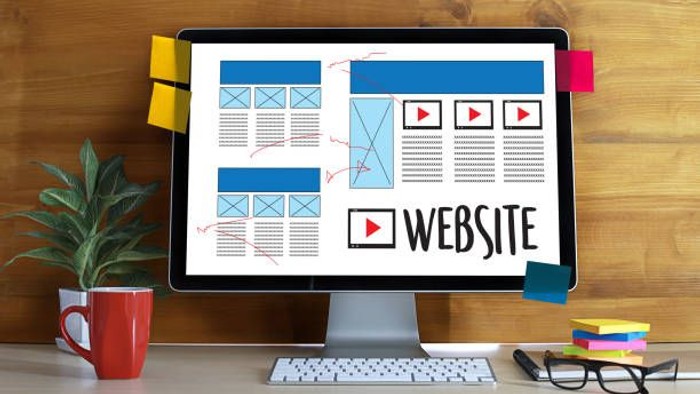 Ein Arbeitsplatz mit einem Computerbildschirm, auf dem ein Website-Layout entworfen wird, sowie Bürobedarf und Pflanzen in der Nähe.