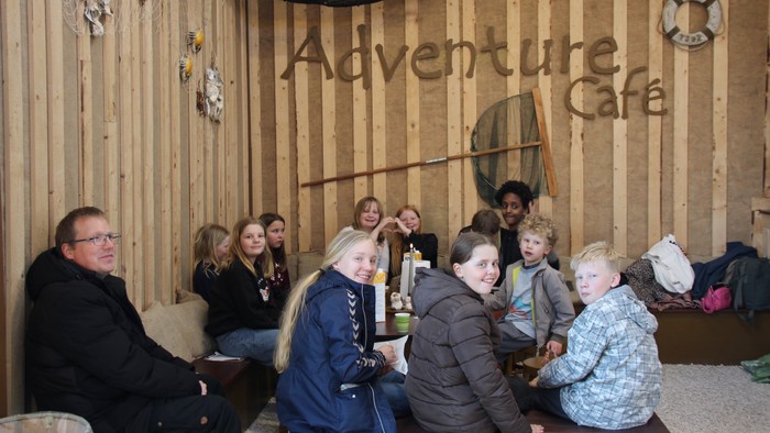 En flok børn, der sidder samlet i en Adventure Café. i baggrunden hænger et rejenet.