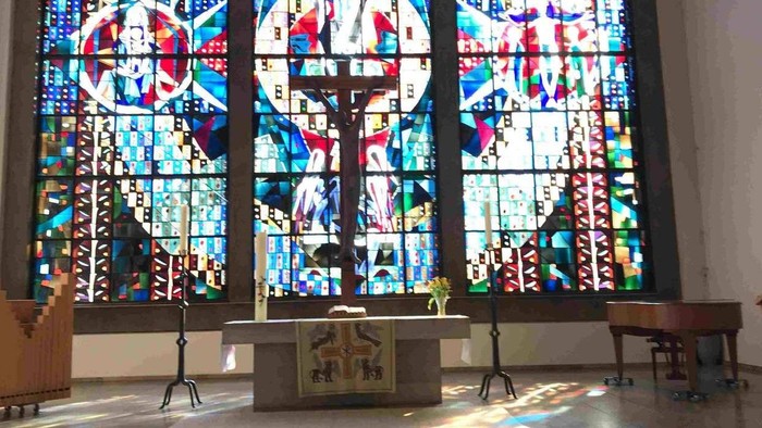 Buntglasfenster erhellen einen ruhigen Kirchenaltar mit hölzernen Kirchenbänken und religiösen Verzierungen.