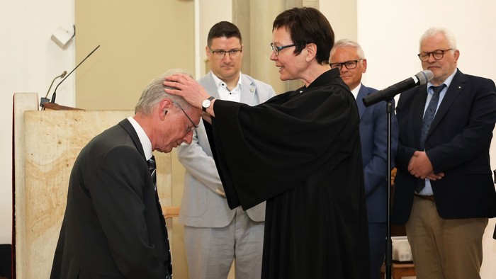 Ein Mann, Andreas Huneke, im Anzug wird von einer Pfarrerin, Presse Adelheid Ruck-Schröder, gesegnet