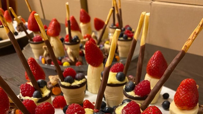 Bunte Dessertspieße mit cremigen Waffeltüten, Beeren, Schokolade und schokoladenüberzogenen Brezeln auf einem Teller.