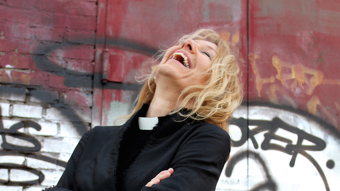 Eine Frau mit blondem Haar lacht vor einer Graffiti-Wand.