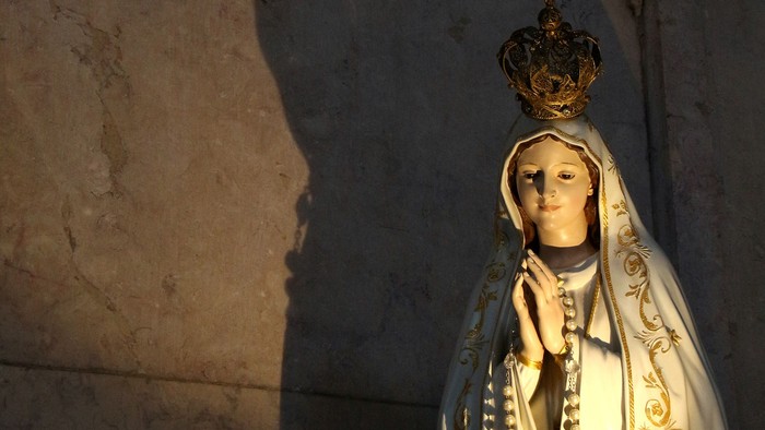 Statue einer bekleideten Figur mit Krone, die einen Schatten an eine Wand wirft