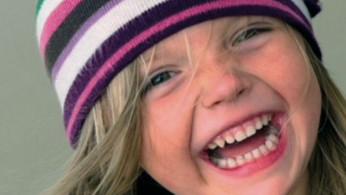 Ein fröhliches Kind mit einer bunten gestreiften Strickmütze lächelt breit.