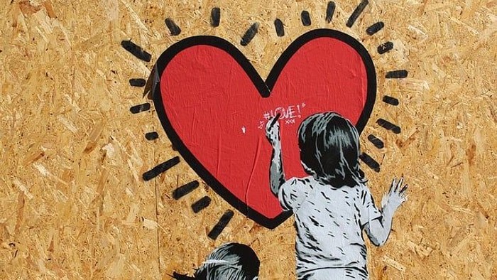 Zwei Kinder malen auf einem großen roten Herz-Mural mit Sonnenstrahlen an einer Holzwand.