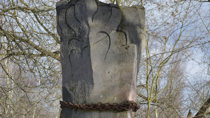 Steinsäule mit aufwendigen Schnitzereien vor einem Baumhintergrund.