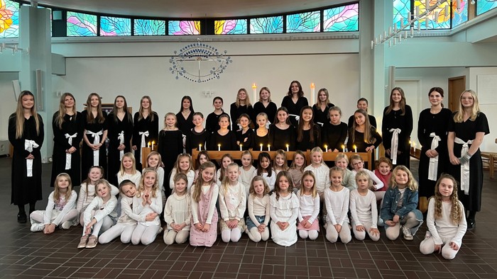 Gruppe af unge kvinder og piger, der holder lys under en formel indendørs ceremoni eller fejring.