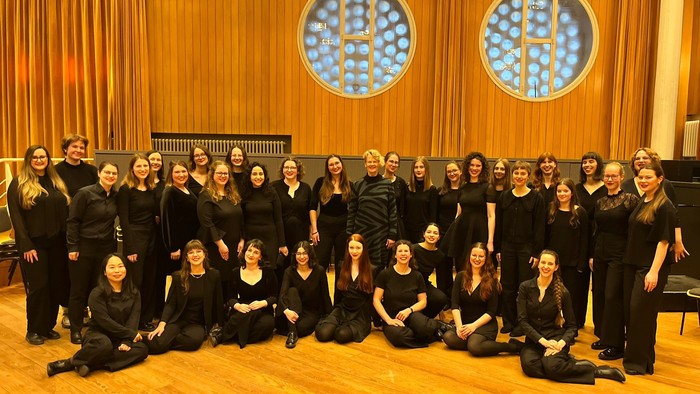 Gruppe von Frauen in abgestimmter schwarzer Kleidung, die gemeinsam in einem Konzertsaal posieren.