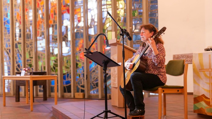 Eine Frau mit Gitarre singt vor einem großen Kirchenfenster