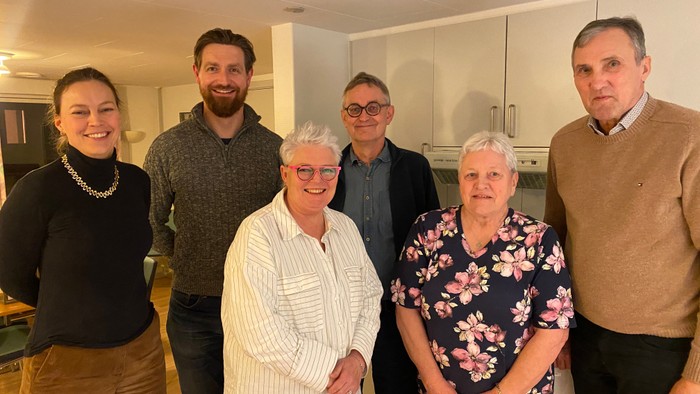 En gruppe af seks personer smiler til kameraet i en køkkenmiljø