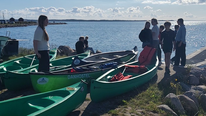 Gruppe bereitet grüne Kajaks für eine Wasseraktivität an einer malerischen Uferlinie vor.