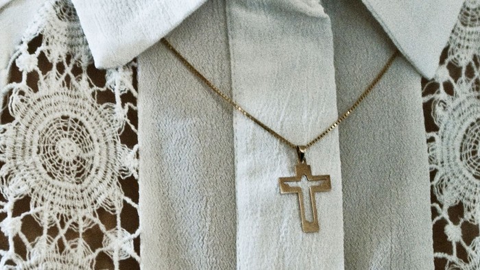 En person iført en hvid skjorte med blondeærmer og et guld korshalskæde.