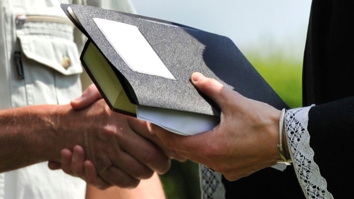 To personer udveksler et indrammet certifikat eller diplom udendørs under en formel begivenhed.