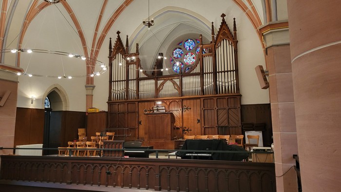 Elegante Kircheninnenausstattung mit einer großen Pfeifenorgel und hölzernen Kirchenbänken unter gewölbten Decken mit Buntglasfenstern.
