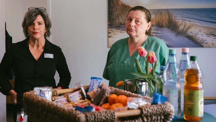 Zwei Frauen stehen neben einem Tisch, der mit Snacks, Getränken und einem Blumenstrauß gedeckt ist.