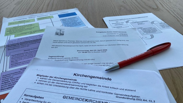 Wahlunterlagen und Formulare für eine Kirchenvorstandssitzung mit einem roten Stift auf einem Holztisch.