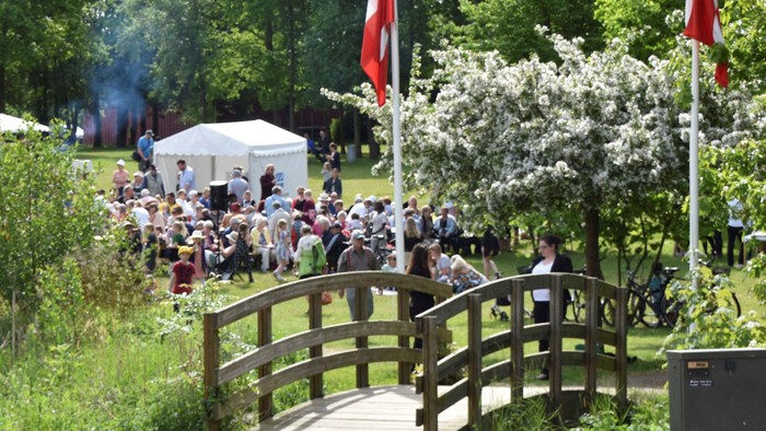 En gruppe af mennesker sidder på græs under tre røde flag.