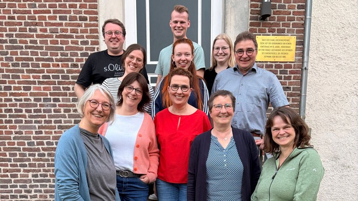 Gruppe von Menschen, die fröhlich vor dem Eingang eines Backsteingebäudes mit Treppen posieren.