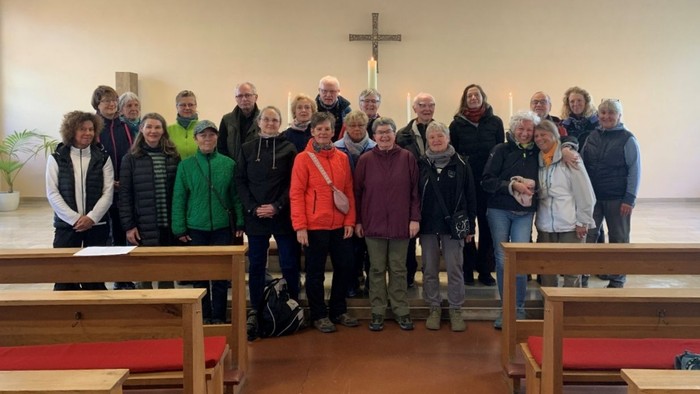 Gruppe von Menschen, die gemeinsam in einer Kirche mit hölzernen Kirchenbänken und einem Kreuz im Hintergrund posieren.