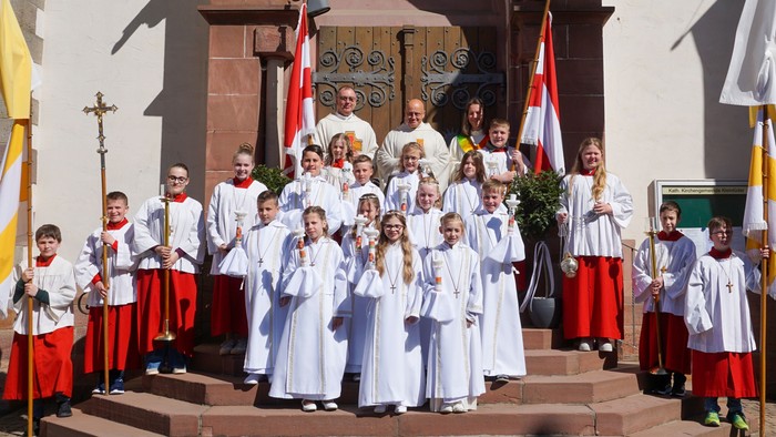 Eine Gruppe von Kindern und Geistlichen in Roben posiert vor dem Eingang einer Kirche während einer offiziellen Veranstaltung.