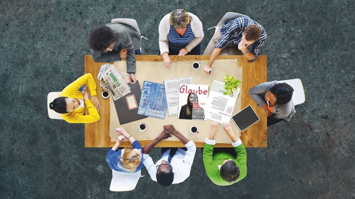 Eine Gruppe von Menschen sitzt um einen Tisch und arbeitet an Projekten.