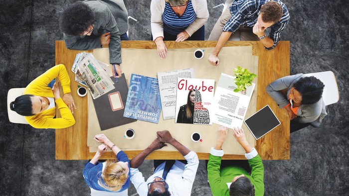 Eine Gruppe von Menschen sitzt um einen Tisch und arbeitet an einem Projekt.
