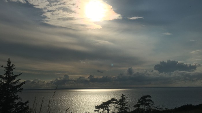 Sollys bryder gennem skyerne over et roligt, glitrende vand ved tusmørke.