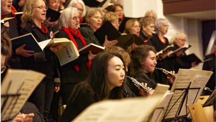 Eine vielfältige Gruppe von Sängerinnen, Sängern und Musikerinnen und Musikern, die gemeinsam in einem Konzert probt oder auftritt.