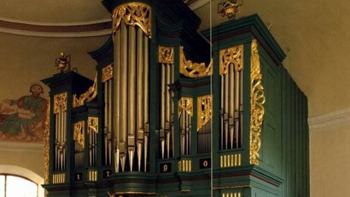 Komplexe historische Pfeifenorgel mit aufwendigen Goldverzierungen und grünen Paneelen in einer Kirche.