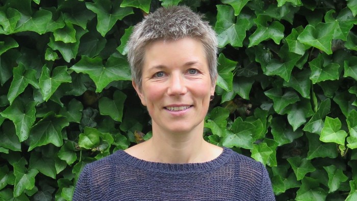 Kvinde med kort hår står foran grønne planter.