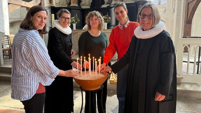 Zwei Schwangere Frauen, zwei Pastorinnen und eine Gynäkologin haben Kerzen angezündet und schauen ins Bild. Sie stehen vor dem Altar in St. Aegidien.
